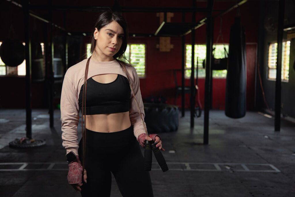 Young female boxer confidently posing in a gym, showcasing fitness and strength.